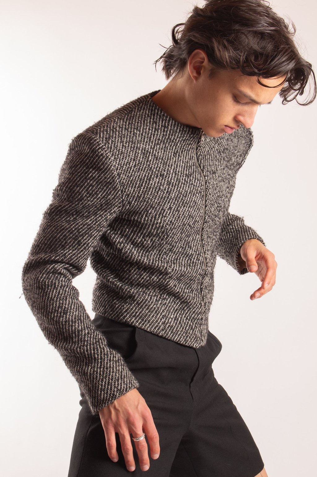 Young man posing in a textured gray tweed jacket and black trousers against a white background.