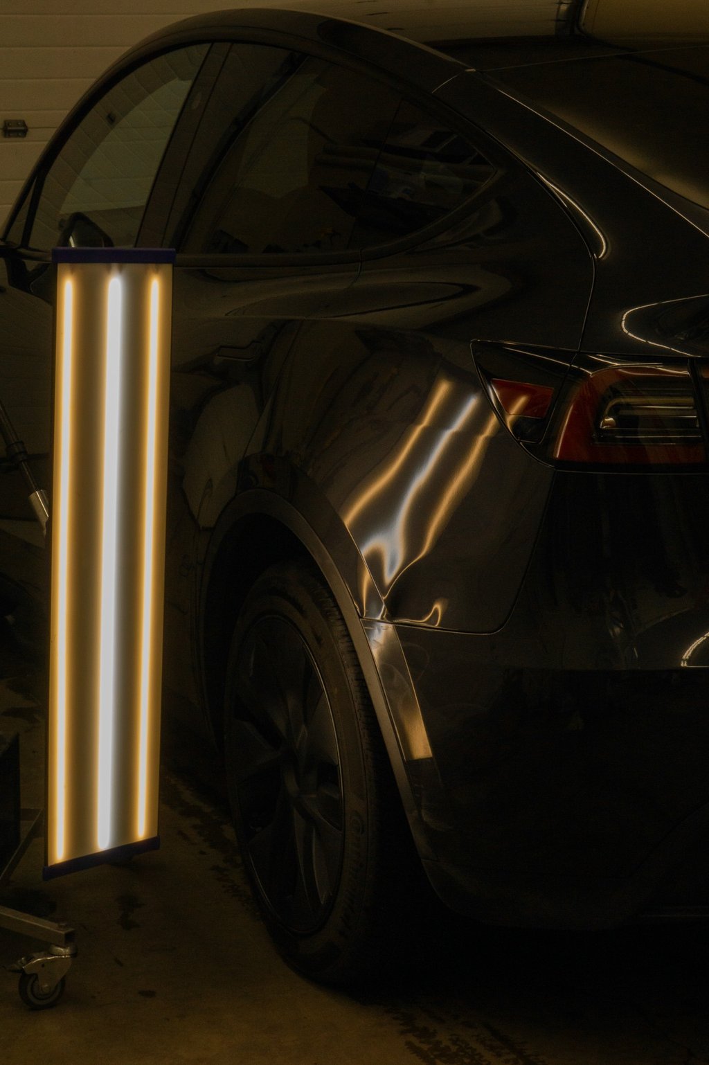 A paintless dent repair light reflecting off a black car to reveal body damage for PDR technicians.