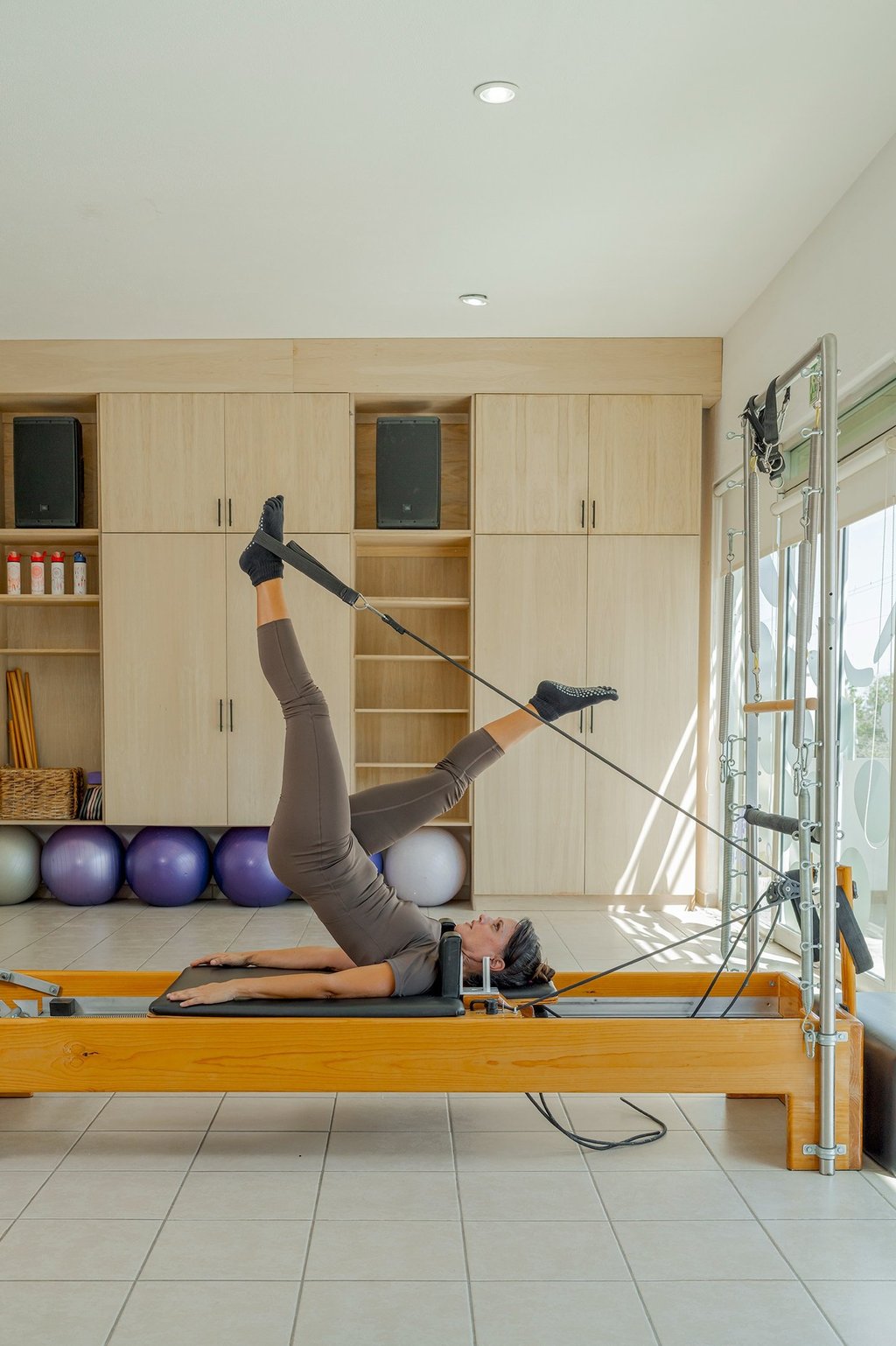 Woman lying on a Pilates Reformer doing a leg exercise using the foot straps in the Cabo San Lucas studio.