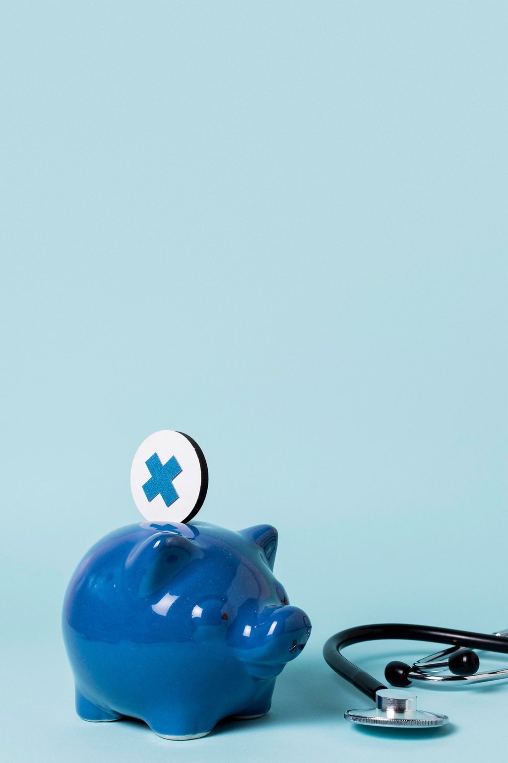 Alcancía azul con moneda de cruz médica y estetoscopio que representan ahorros y costos en el seguro