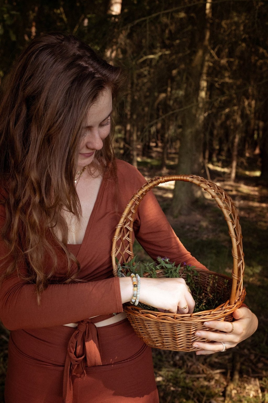 Eine Frau sammelt Kräuter in einem Korb, während sie in einem Wald steht.