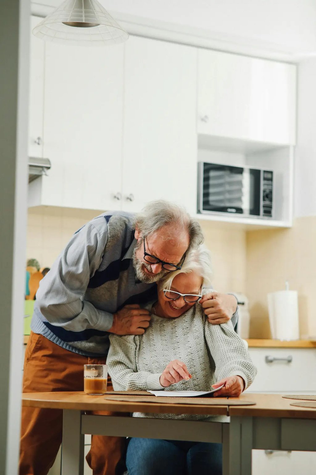 A happy senior couple at home in a bright kitchen reviewing financial documents together at a wooden table.