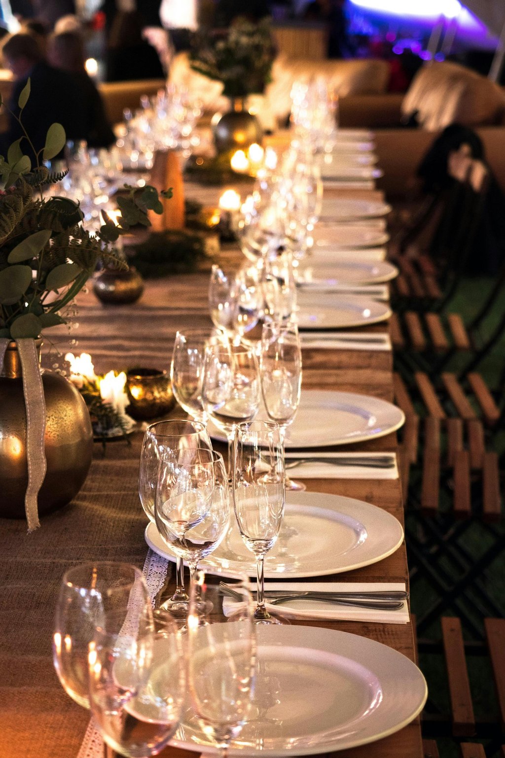 Elegant long wooden banquet table set with white plates, wine glasses, and candles for a wedding reception.