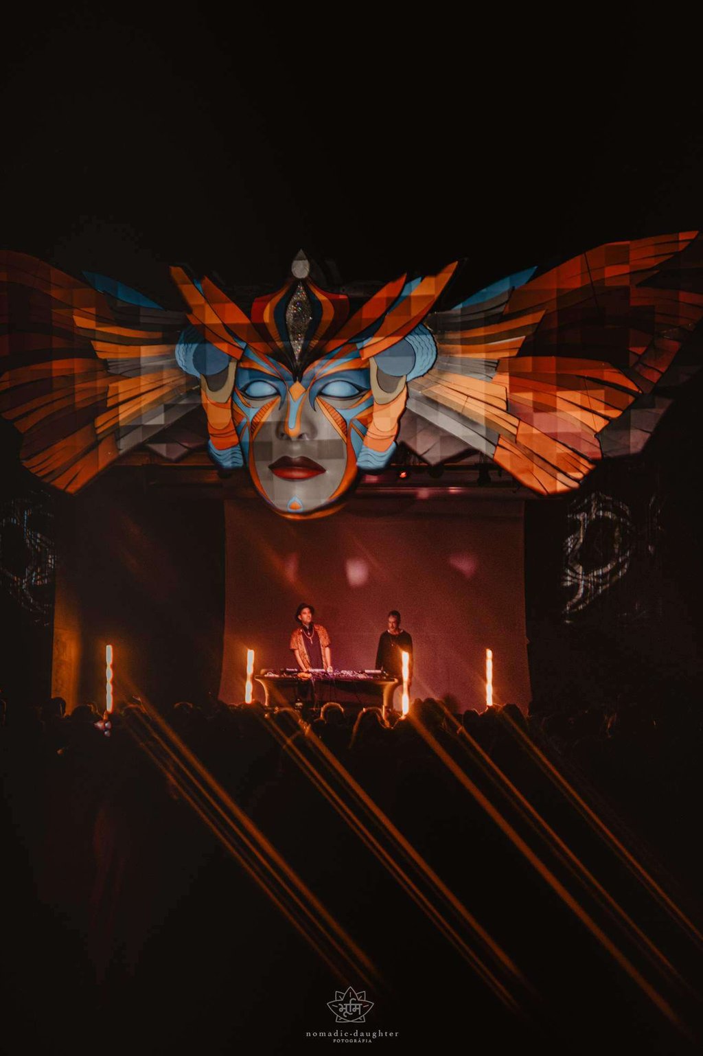 DJs performing atBUMI festival under a large, illuminated tribal mask stage installation.