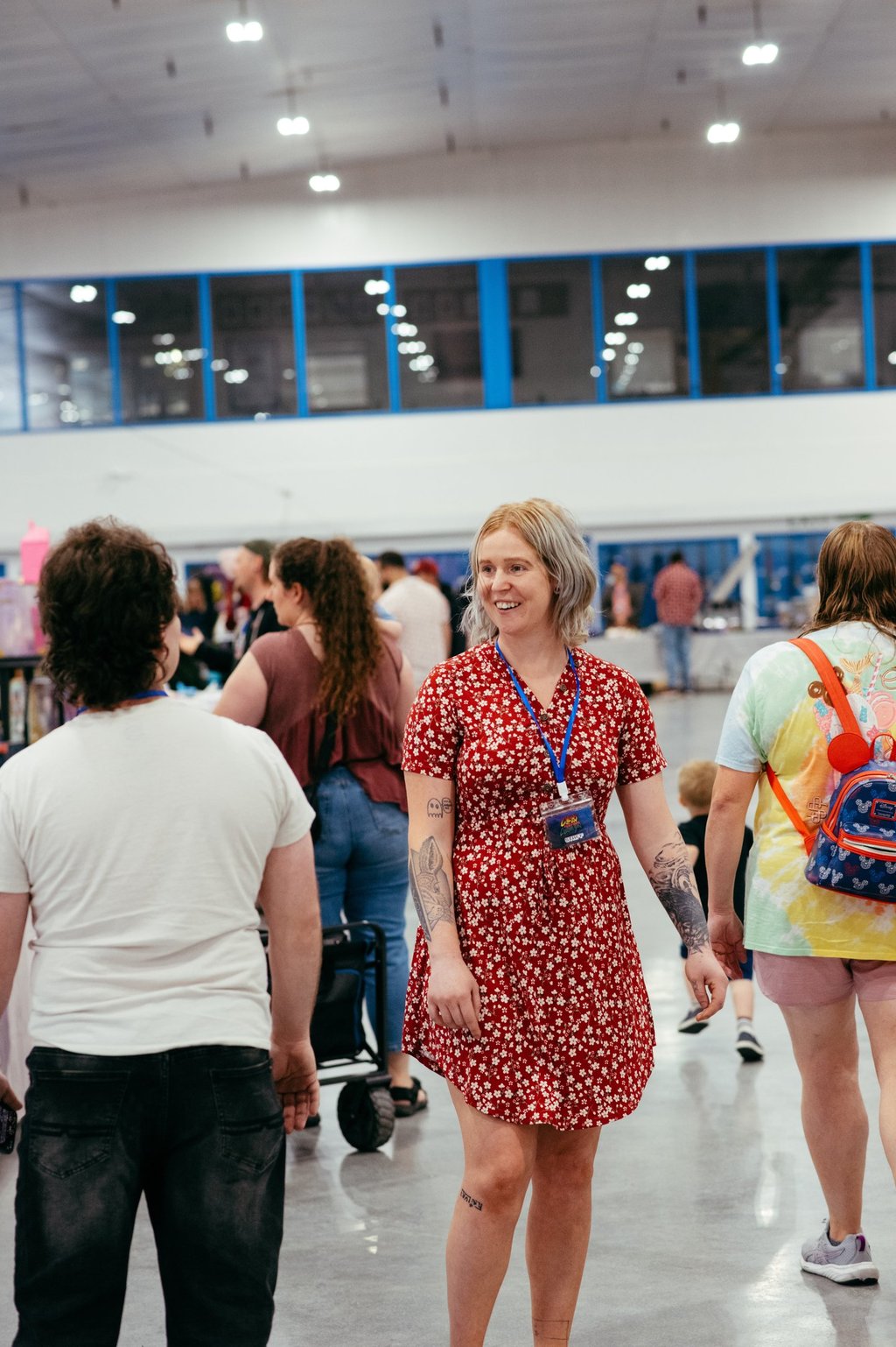 A woman in a red dress with a volunteer badge smiles at event goers