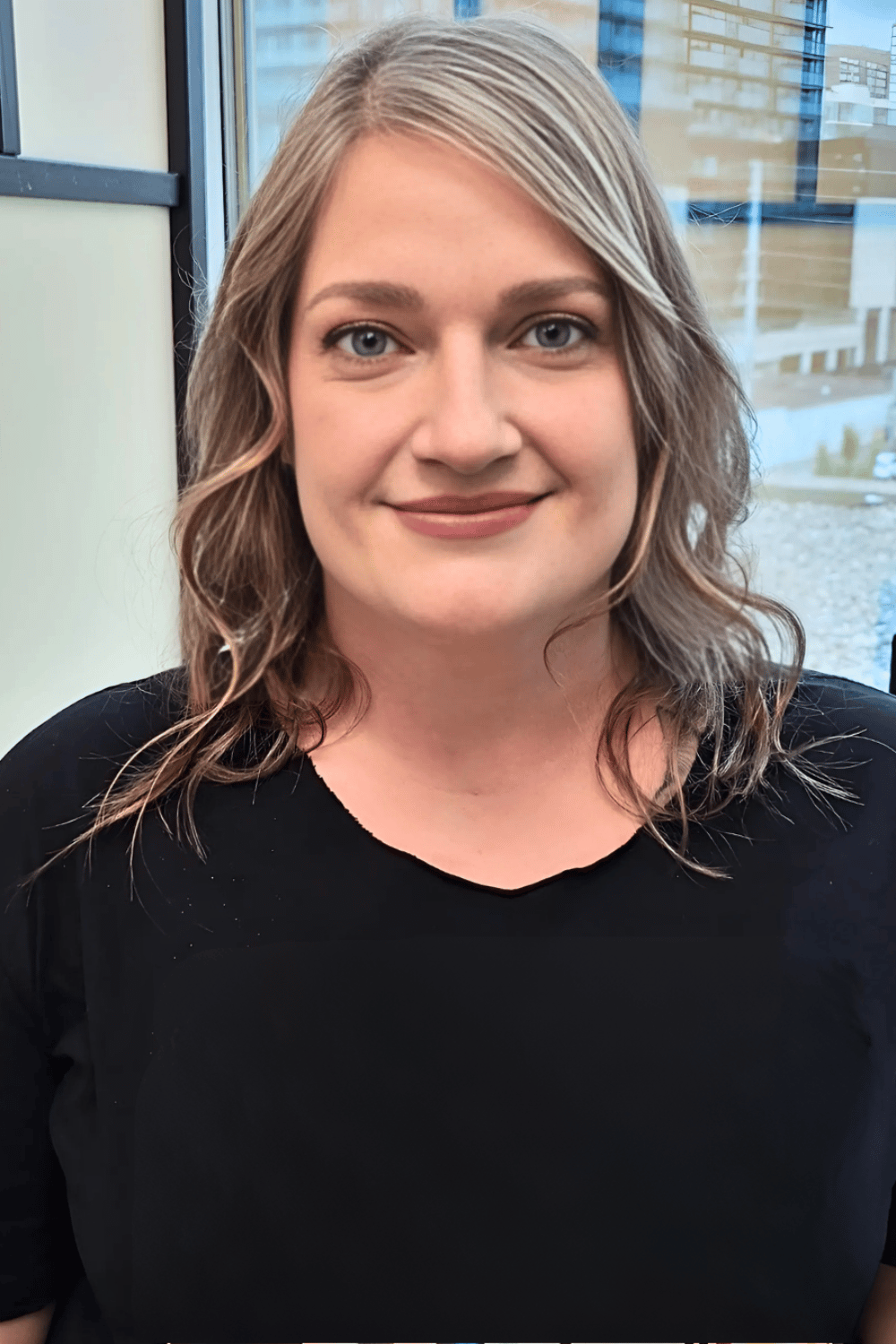 Professional portrait of a smiling woman with wavy blonde hair wearing a black shirt.