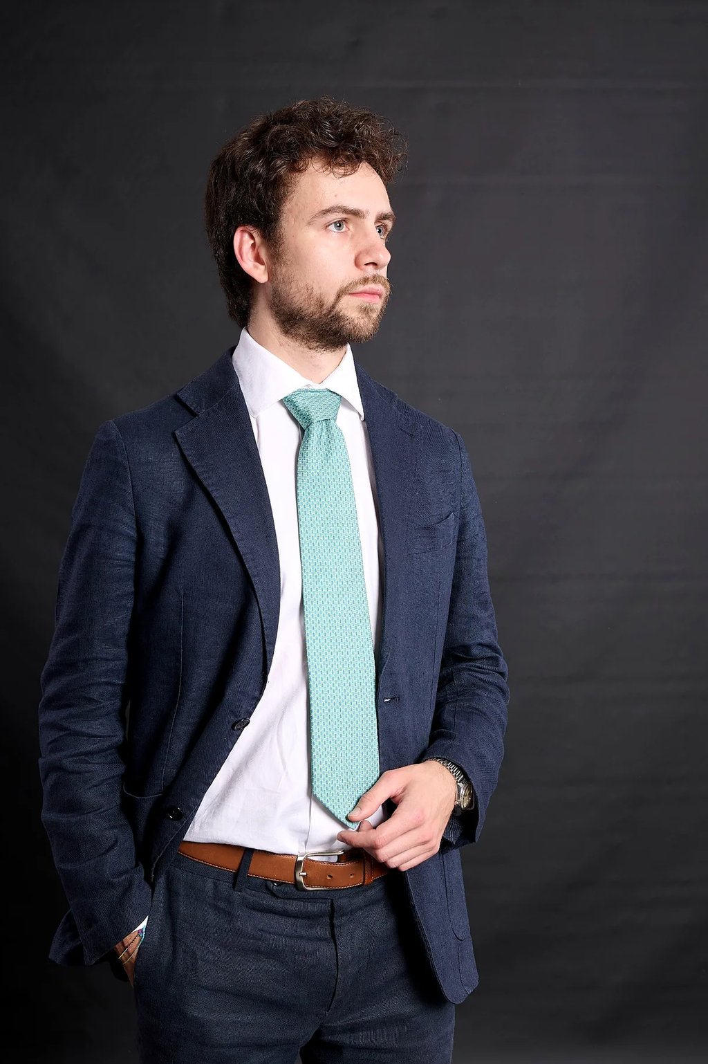 Professional man wearing a navy blue suit with a light teal patterned tie against a dark background.