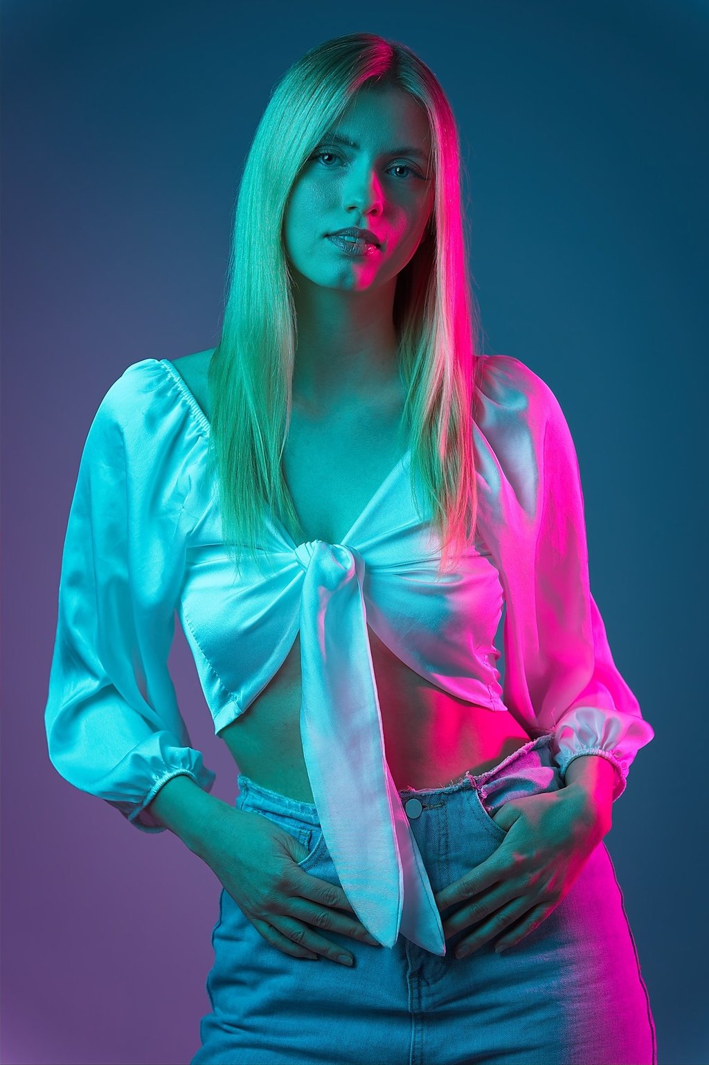 Portrait einer Frau mit weißer Bluse und Jeans vor farbig beleuchtetem Hintergrund