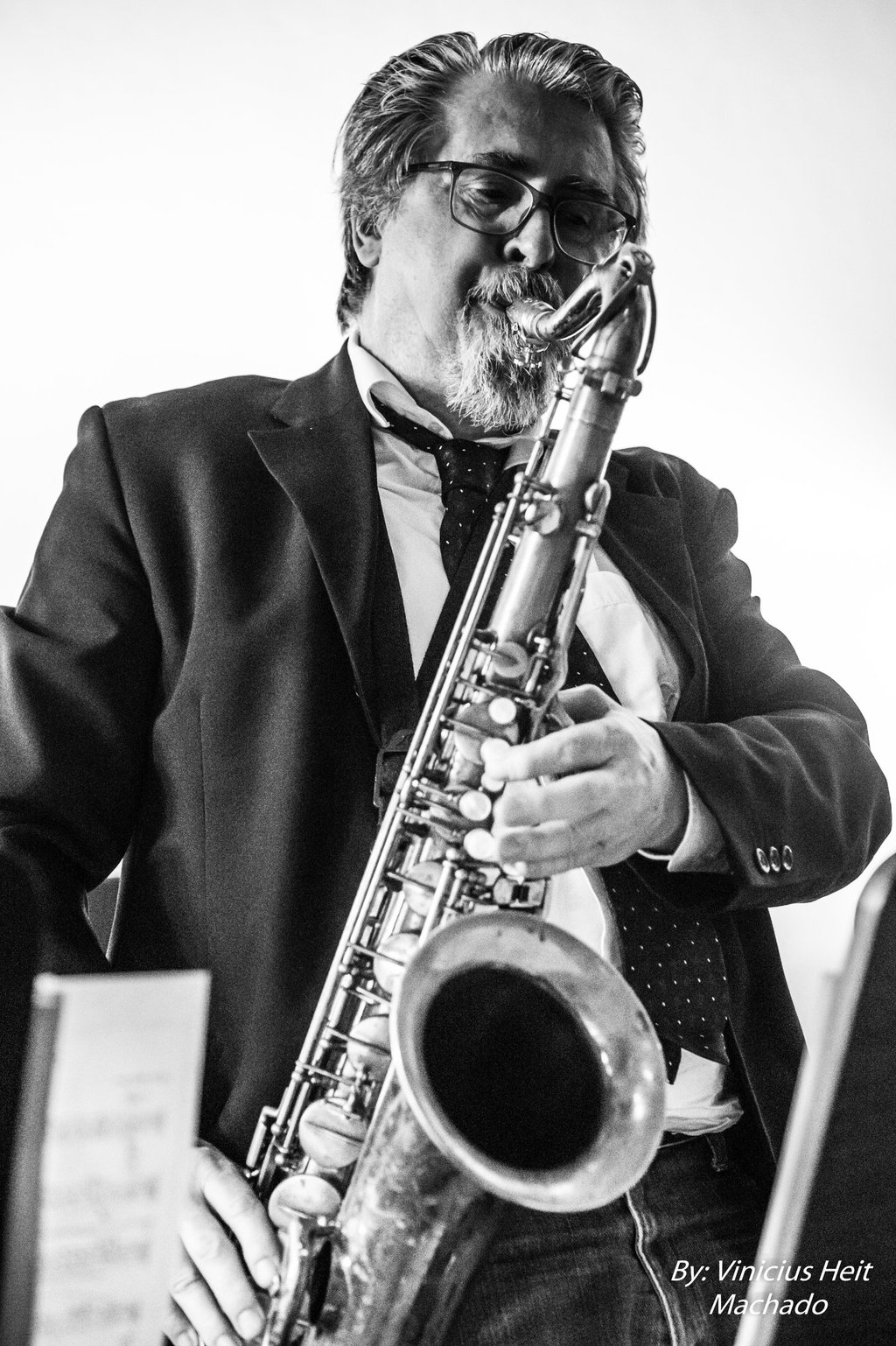 Black and white photo of a male jazz musician in a suit playing the tenor saxophone.