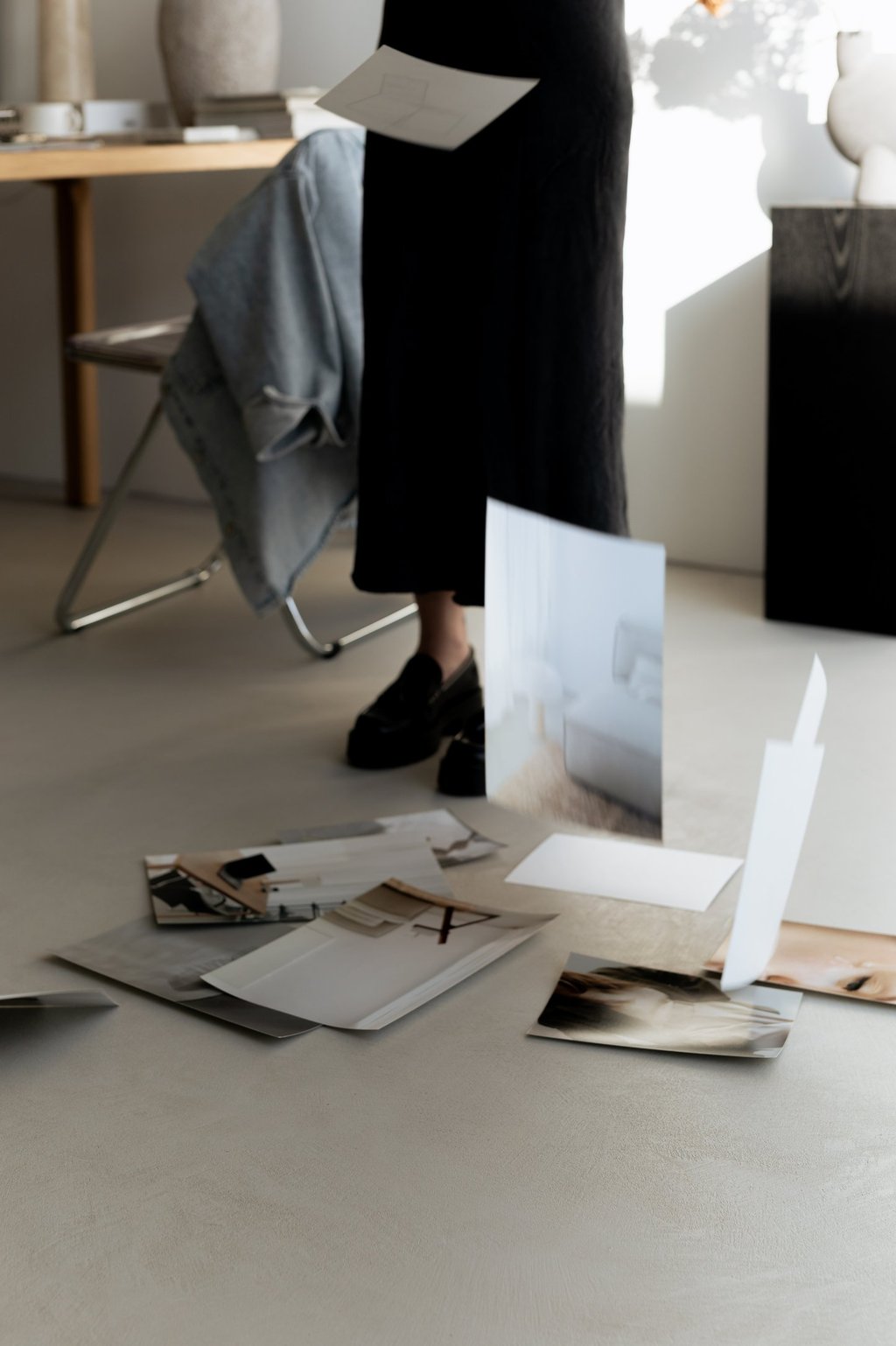 A woman in a minimalist studio dropping photography prints onto the floor for a mood board design.