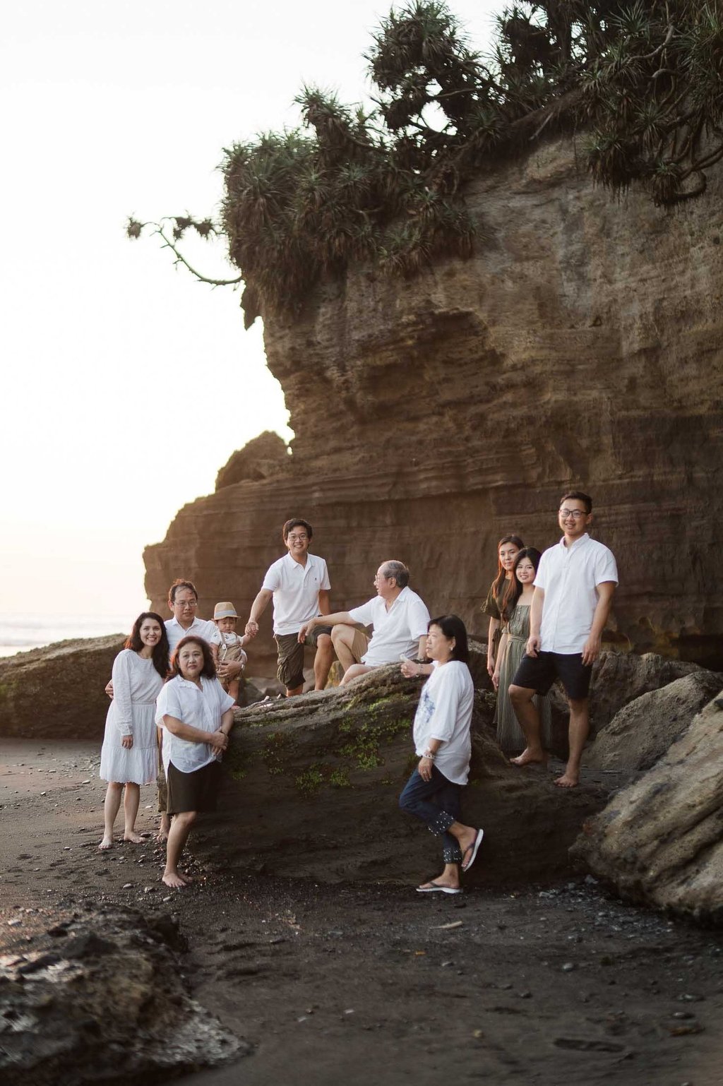 Multi generation family sitting together on coastal rocks at Nyanyi Beach Tabanan Bali during a lifestyle family photography 