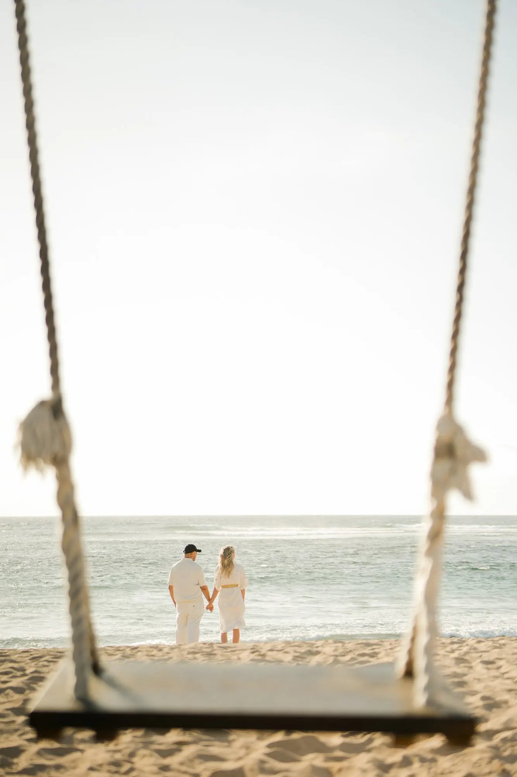 Family framed by a beach swing during a family photography session at Ayodya Resort Bali in Nusa Dua