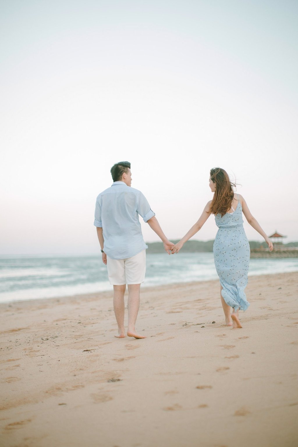 Intimate couple walking hand in hand along shoreline at Sofitel Bali Nusa Dua Beach Resort.