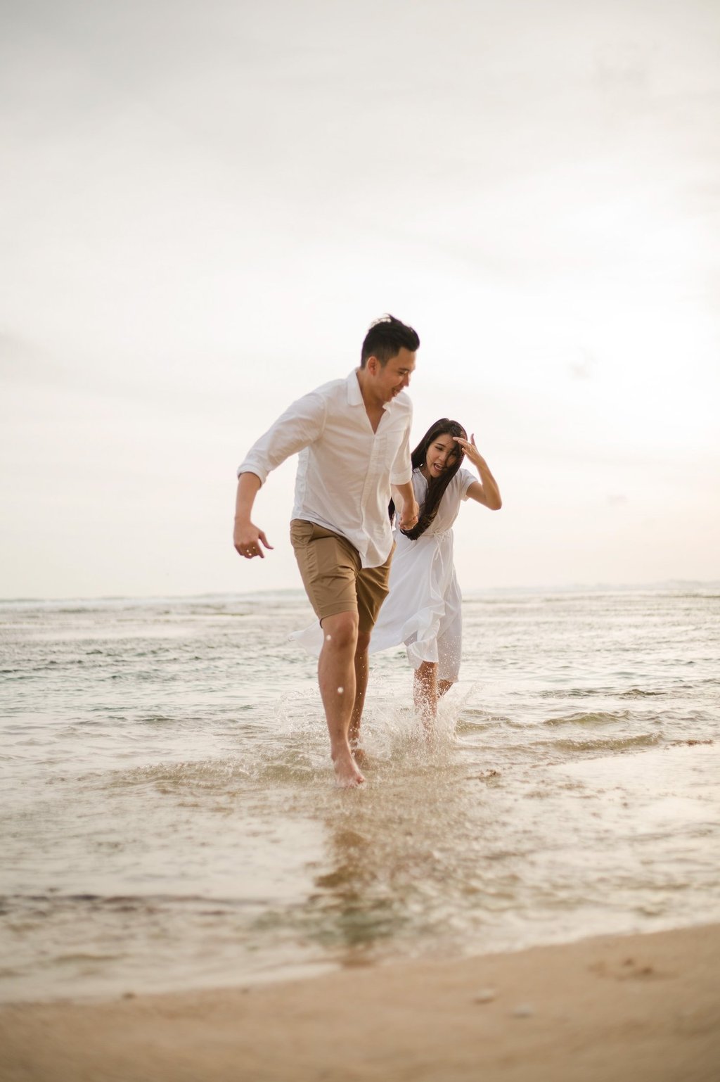 Couple running together in the ocean during proposal photoshoot at Melasti Beach Bali