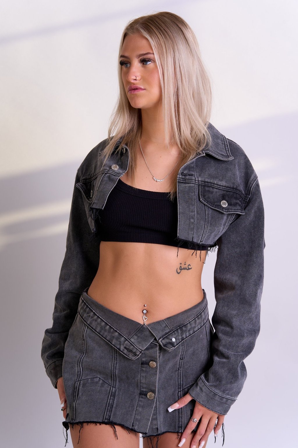 A blonde model wearing a black top and a grey denim cropped jacket and skirt