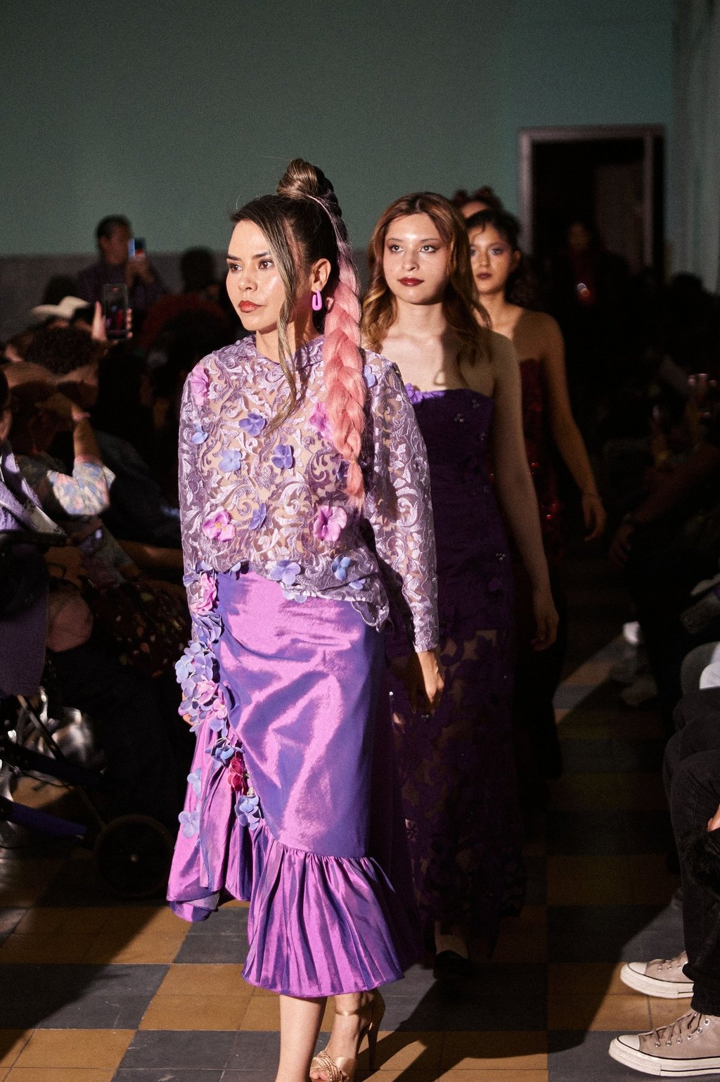 Fashion model wearing a purple lace floral blouse and silk skirt during a runway show.