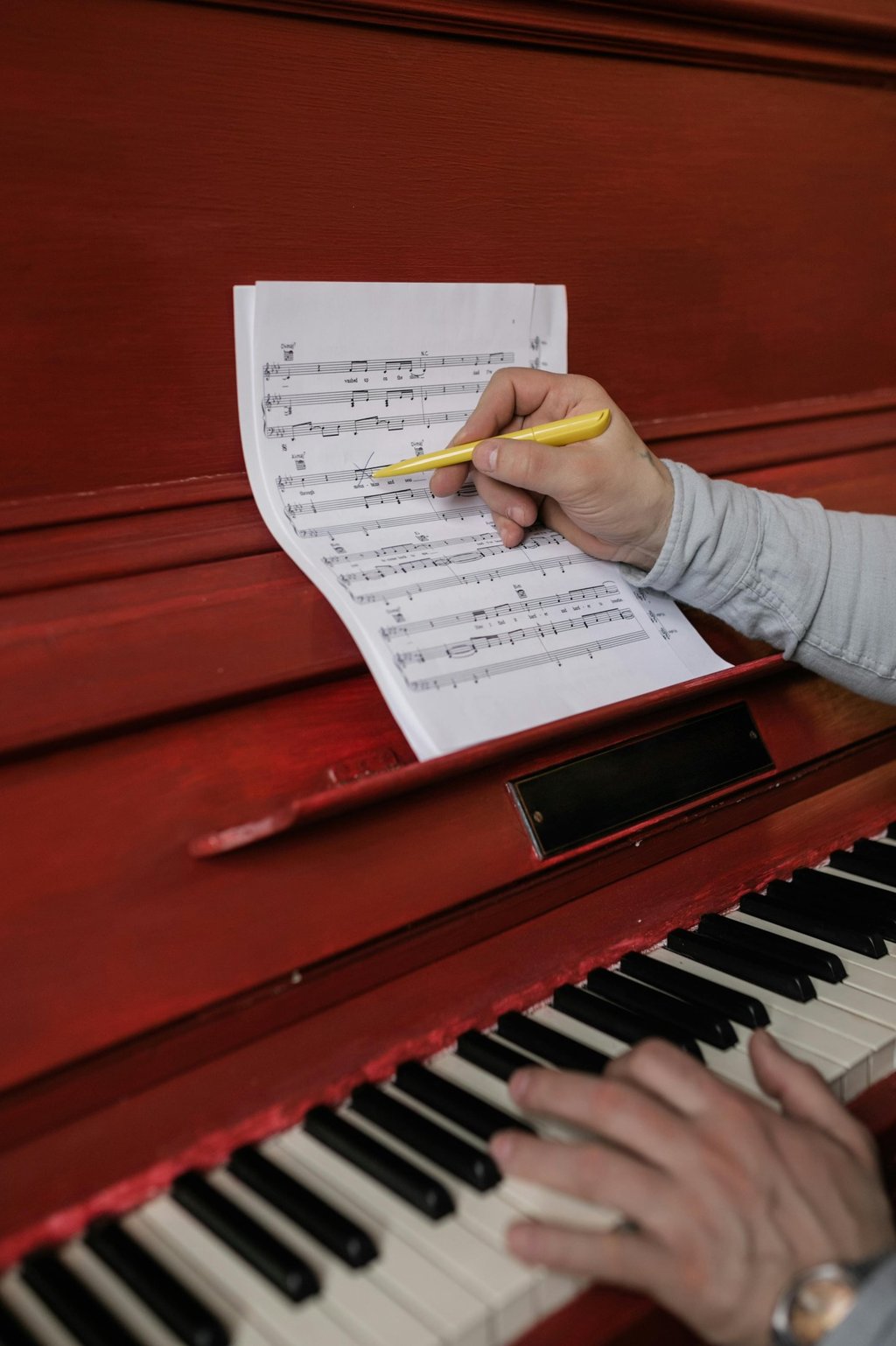 Musician composing music on a red piano while holding a yellow pen over sheet music.