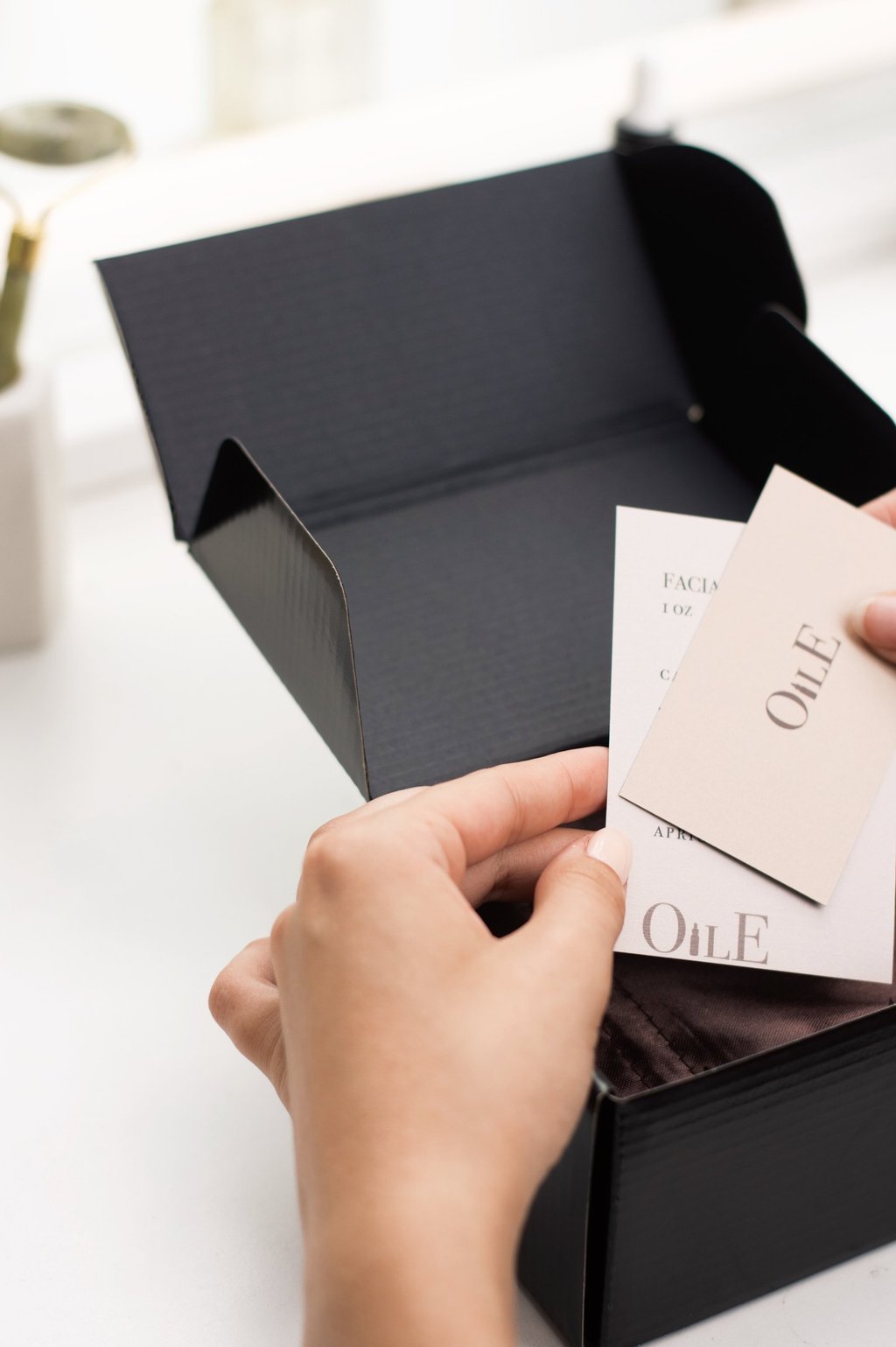 Hands opening a black luxury skincare gift box with Oile brand facial product cards.