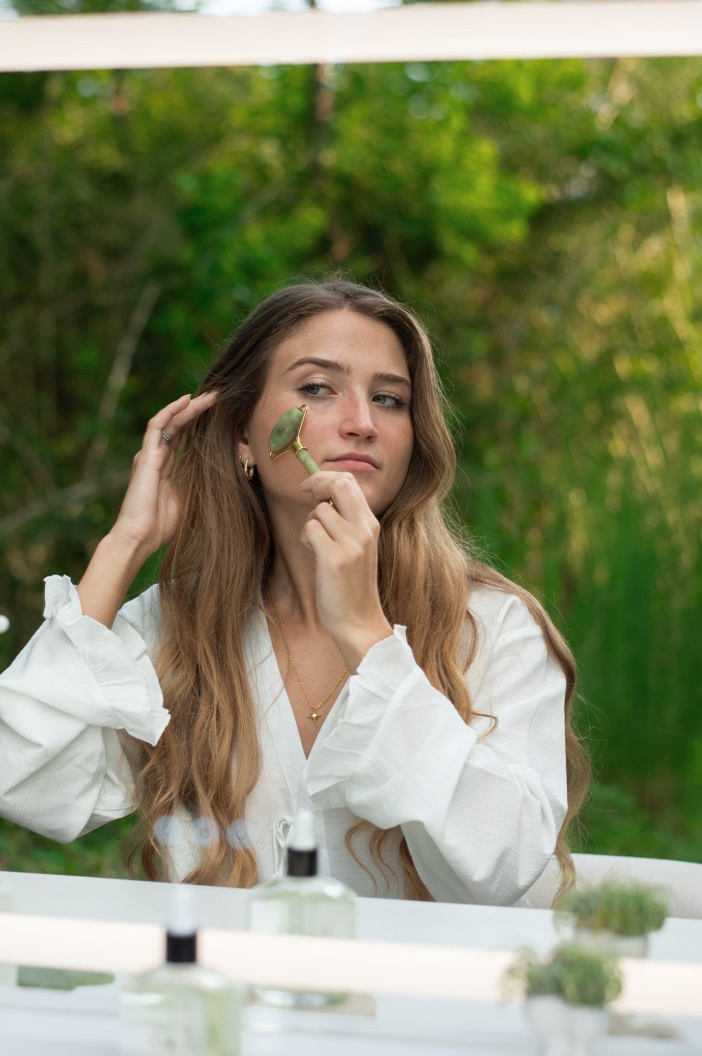 A woman uses a green jade roller for a facial massage and skincare routine.