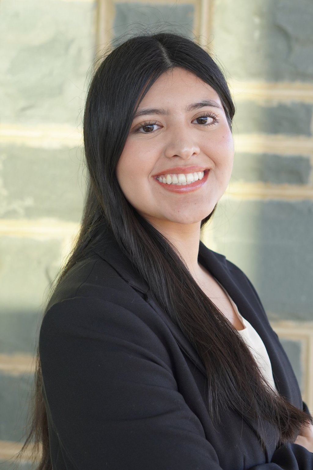 Smiling professional woman with long dark hair wearing a black blazer in a business headshot.