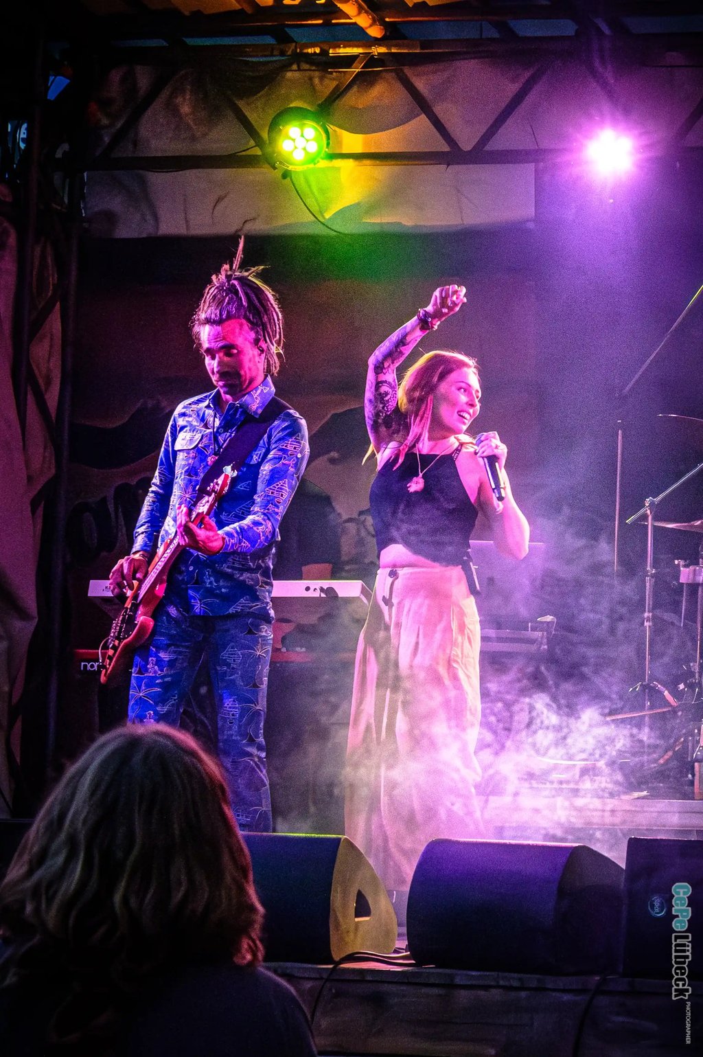 Live band performing on stage with a female singer and bass guitarist under purple and green stage lights.
