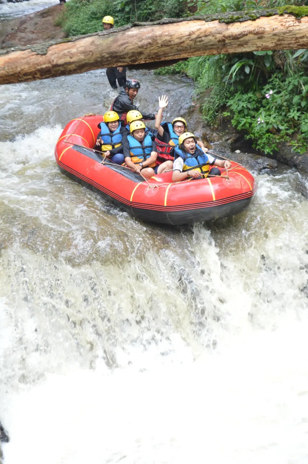 Sekelompok orang di atas perahu karet merah sedang berarung jeram menuruni jeram sungai.