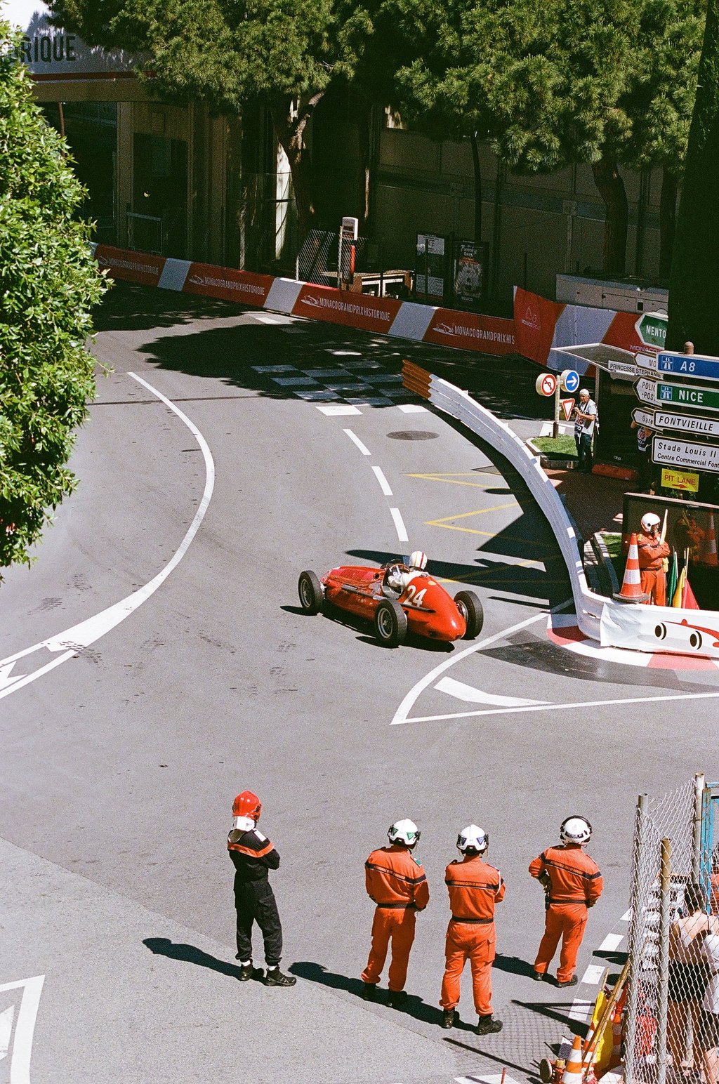 a group of race marshals watching a red race car go through a corner
