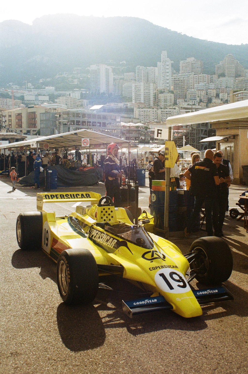a yellow 80's Formula 1 car with a number of people standing around it