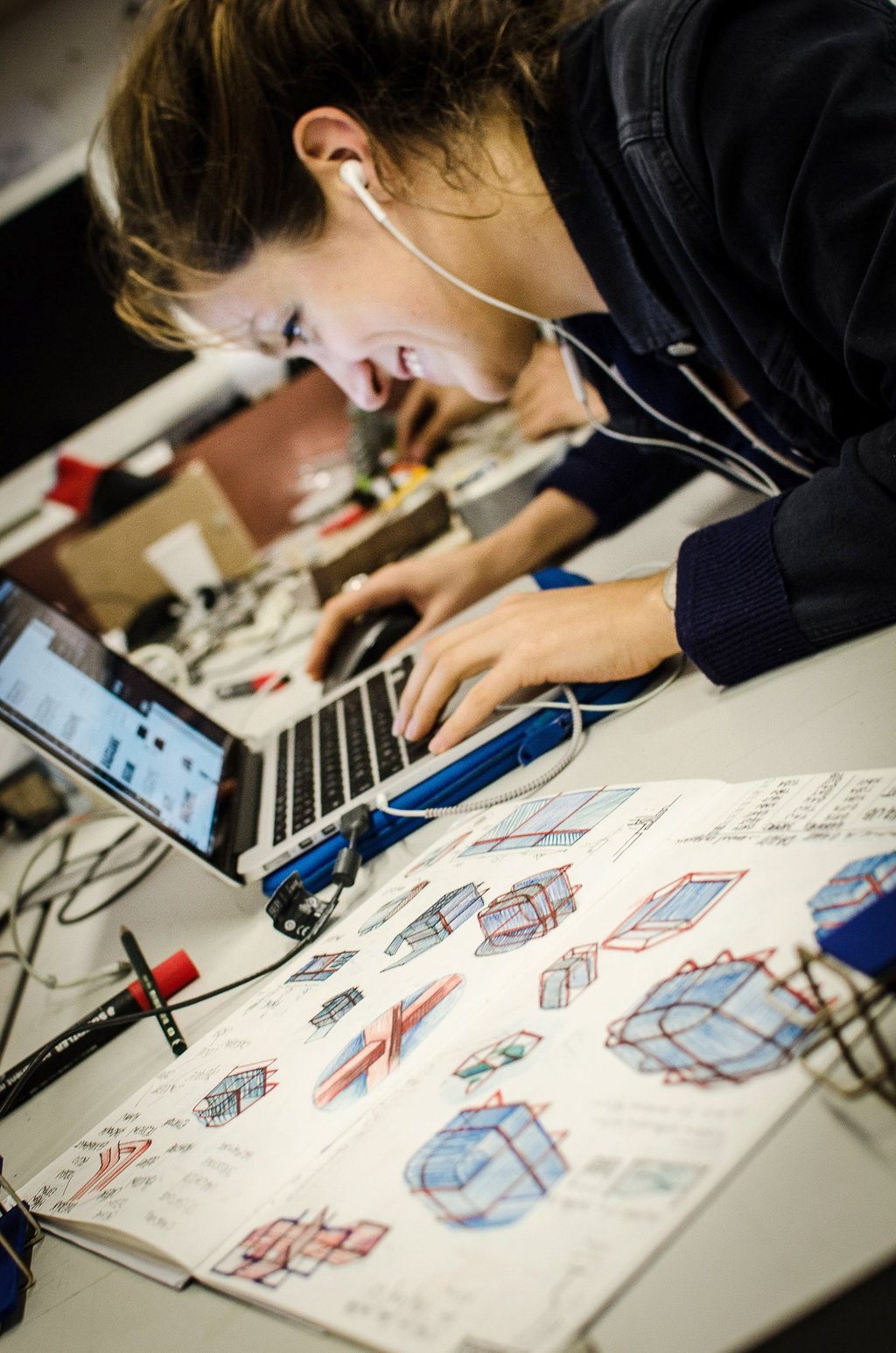 A design student sketching industrial concepts next to a laptop in a creative workspace.