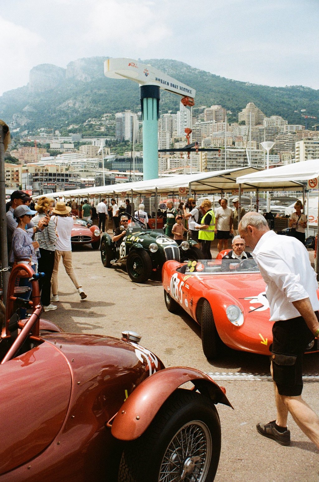 a man in a white shirt and black shorts is walking across of a group of race cars in the paddoc