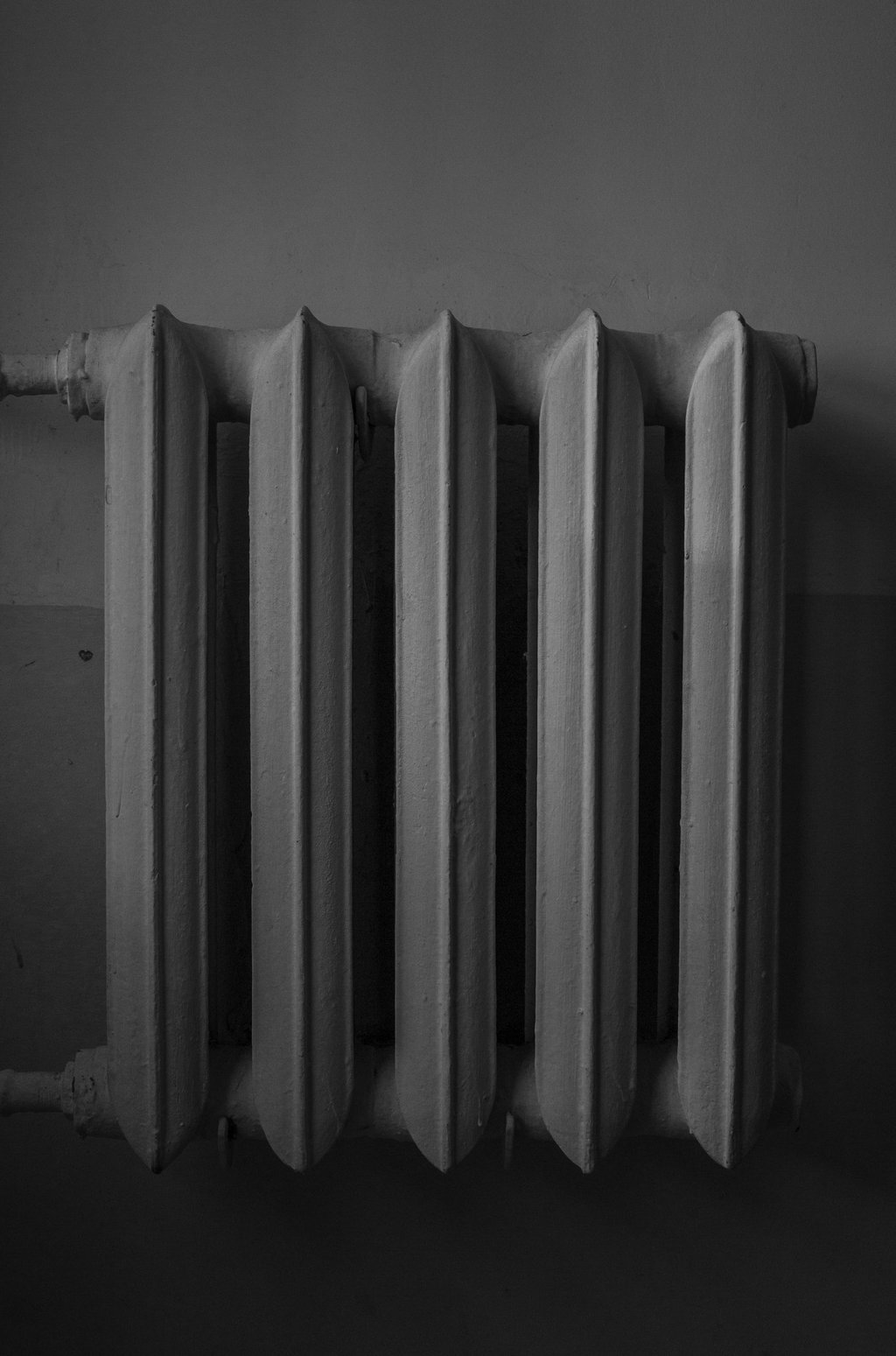 Monochrome image of a cast iron radiator against a wall.