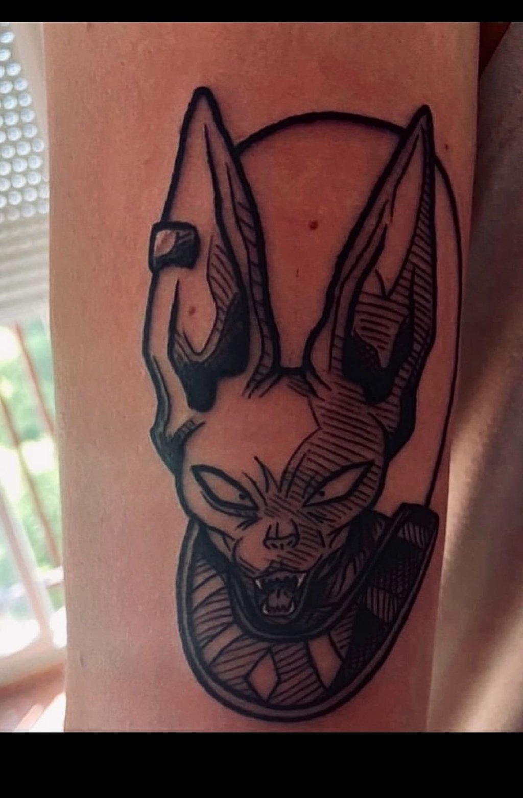 A detailed black and white tattoo of Beerus, the God of Destruction from Dragon Ball Super, with his signature smirk and