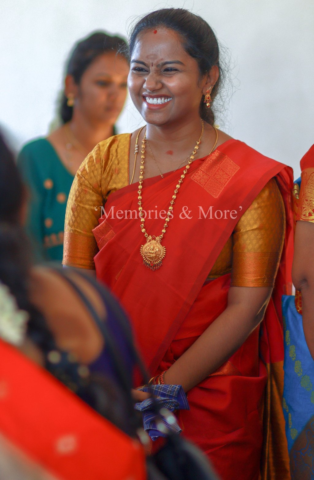 A woman in a red silk saree smiling at a wedding candid photograph by Memories and More Photography