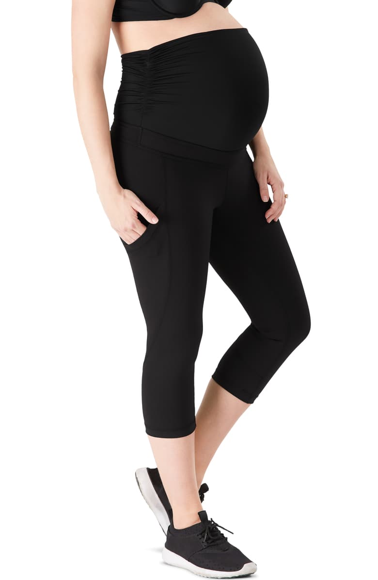 Pregnant woman wearing black maternity capri leggings with side pockets and over-the-belly support.