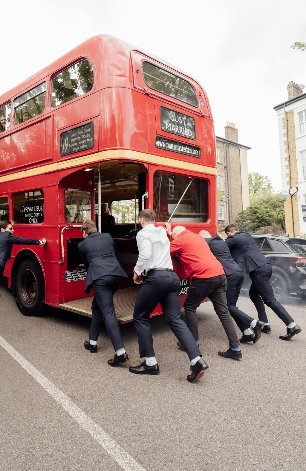 men pushing red bus Just married up the hill