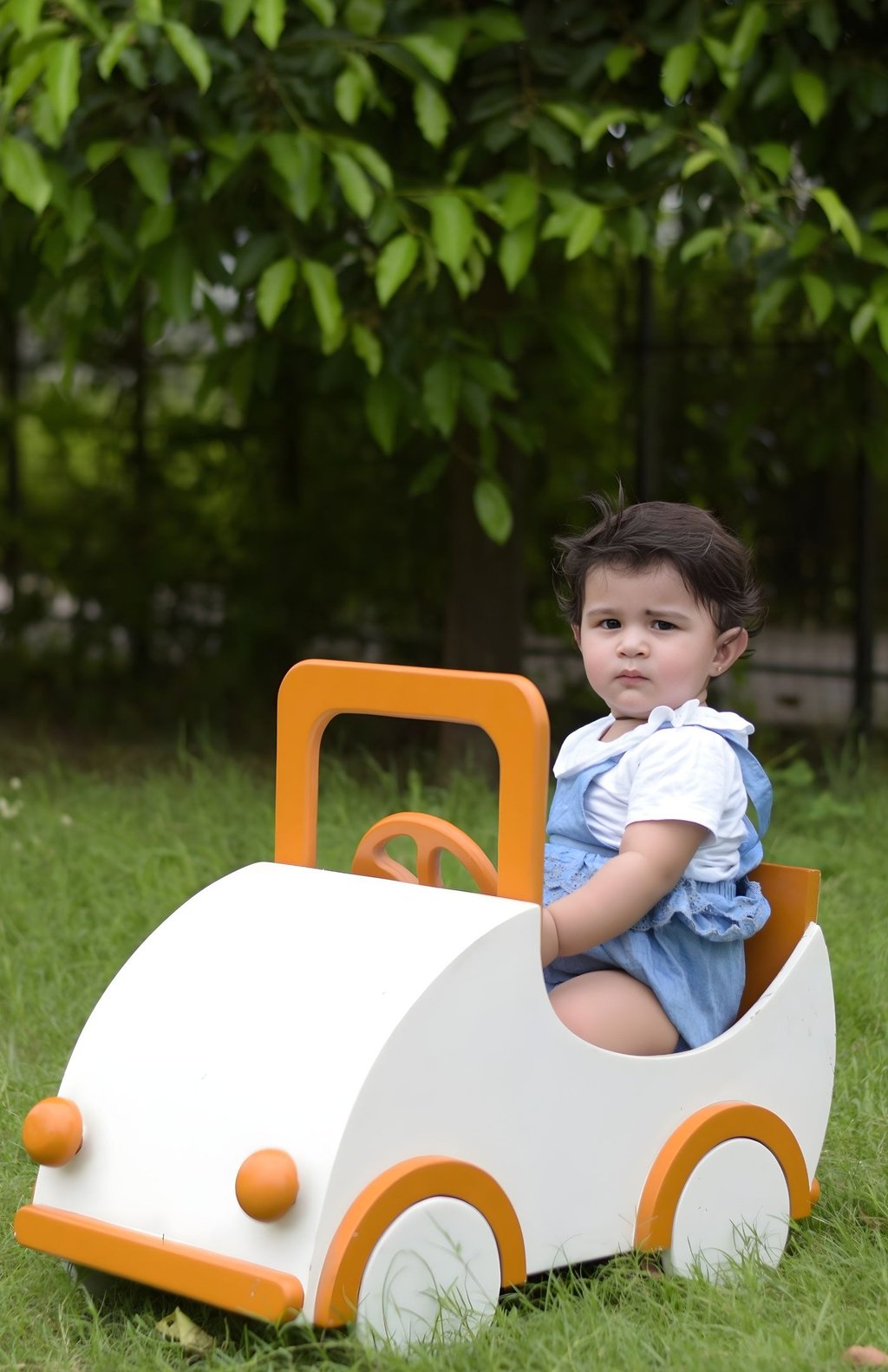 Toddler playing in a white and orange wooden toy car. Milestone photography