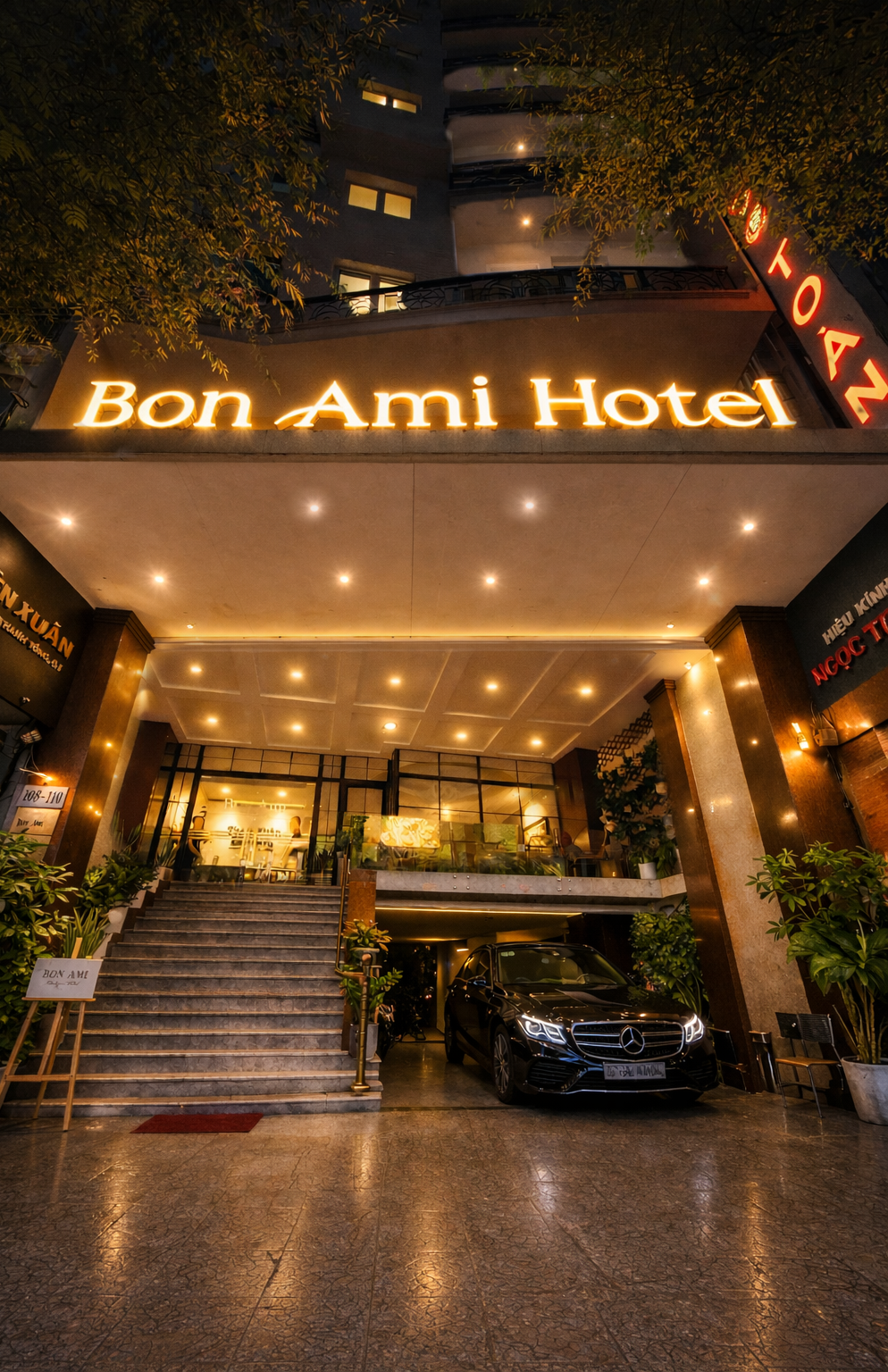 Illuminated entrance of the Bon Ami Hotel in Ho Chi Minh City at night with a luxury car parked out front.