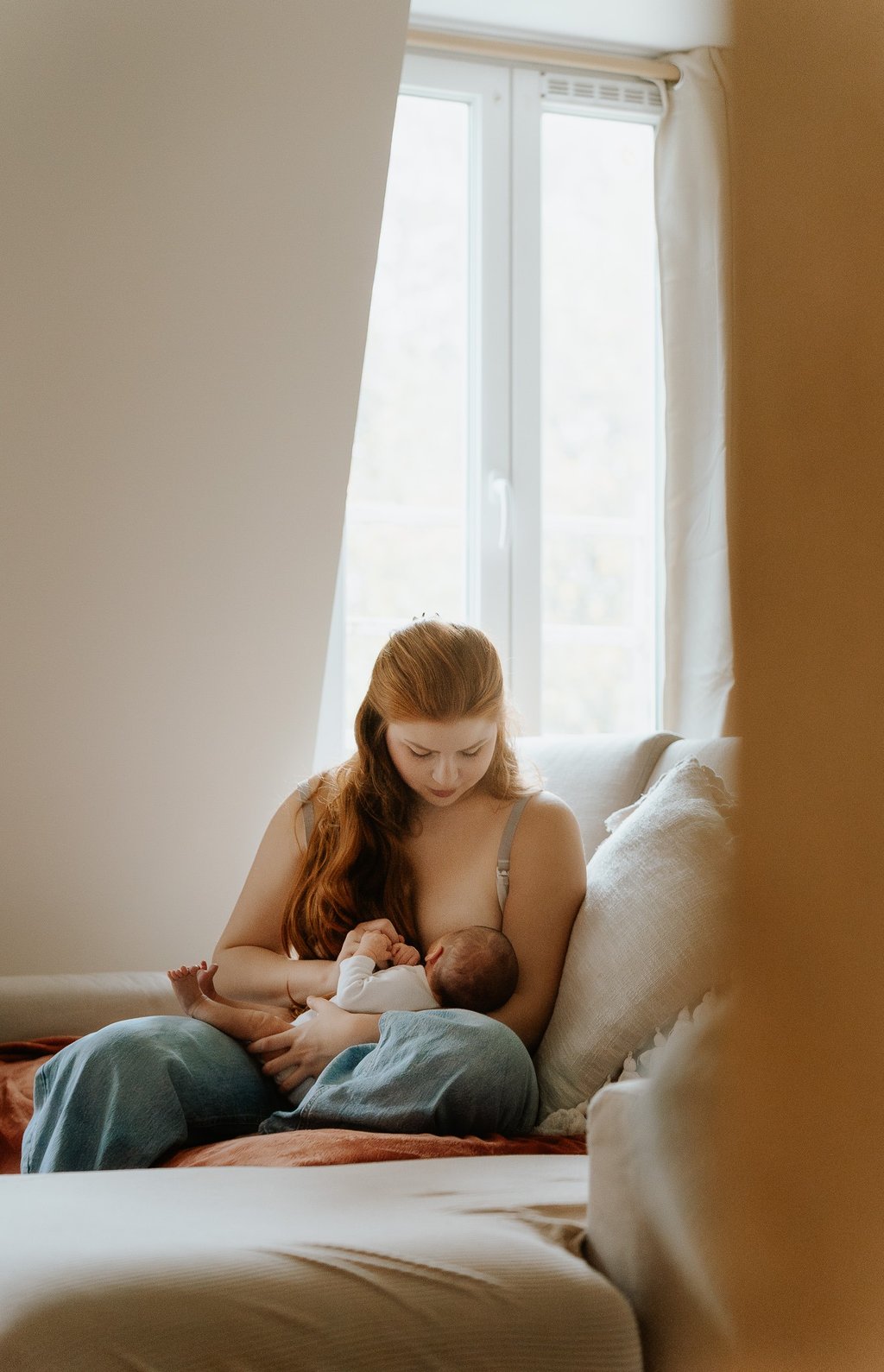 portrait de maman allaitant son nouveau né assise sur son canapé lumière douce en intérieur