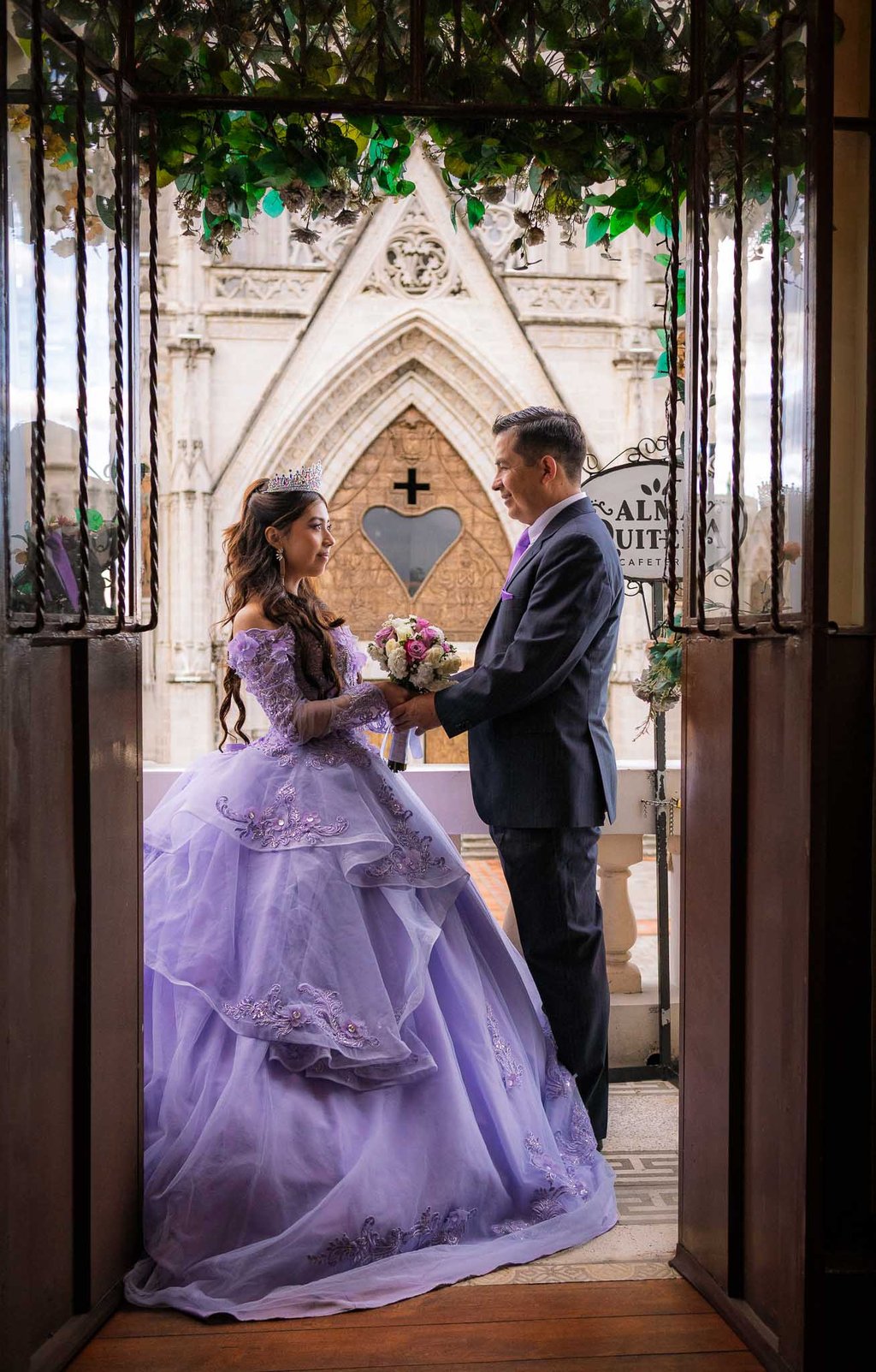 Padre e hija mirándose en marco de balcón por los 15 años en centro histórico de Quito
