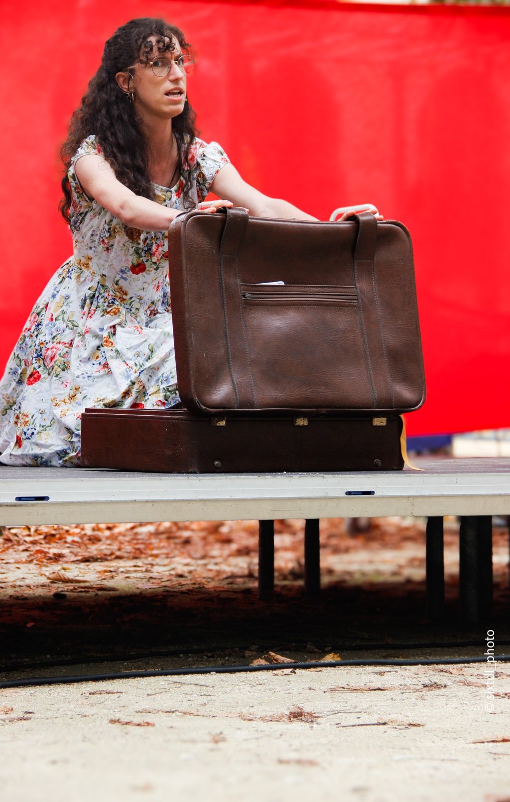 comédienne chanteuse sur scène équipée d'un micro serre tête, en train d'ouvrir une valise