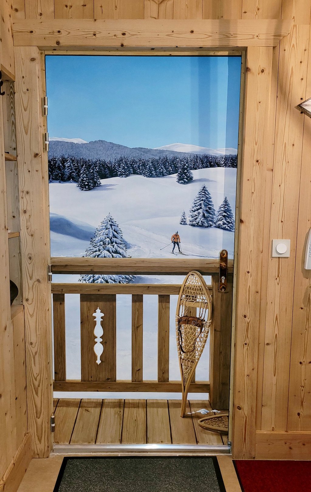 Une porte d'entrée basique se transforme en décor hivernal jurassien. Ce décor habille une porte de service disgracieuse.