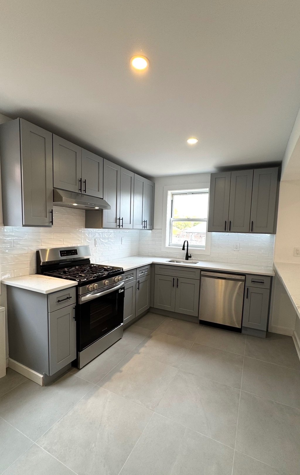 Modern kitchen with grey shaker cabinets, white quartz countertops, and stainless steel appliances.