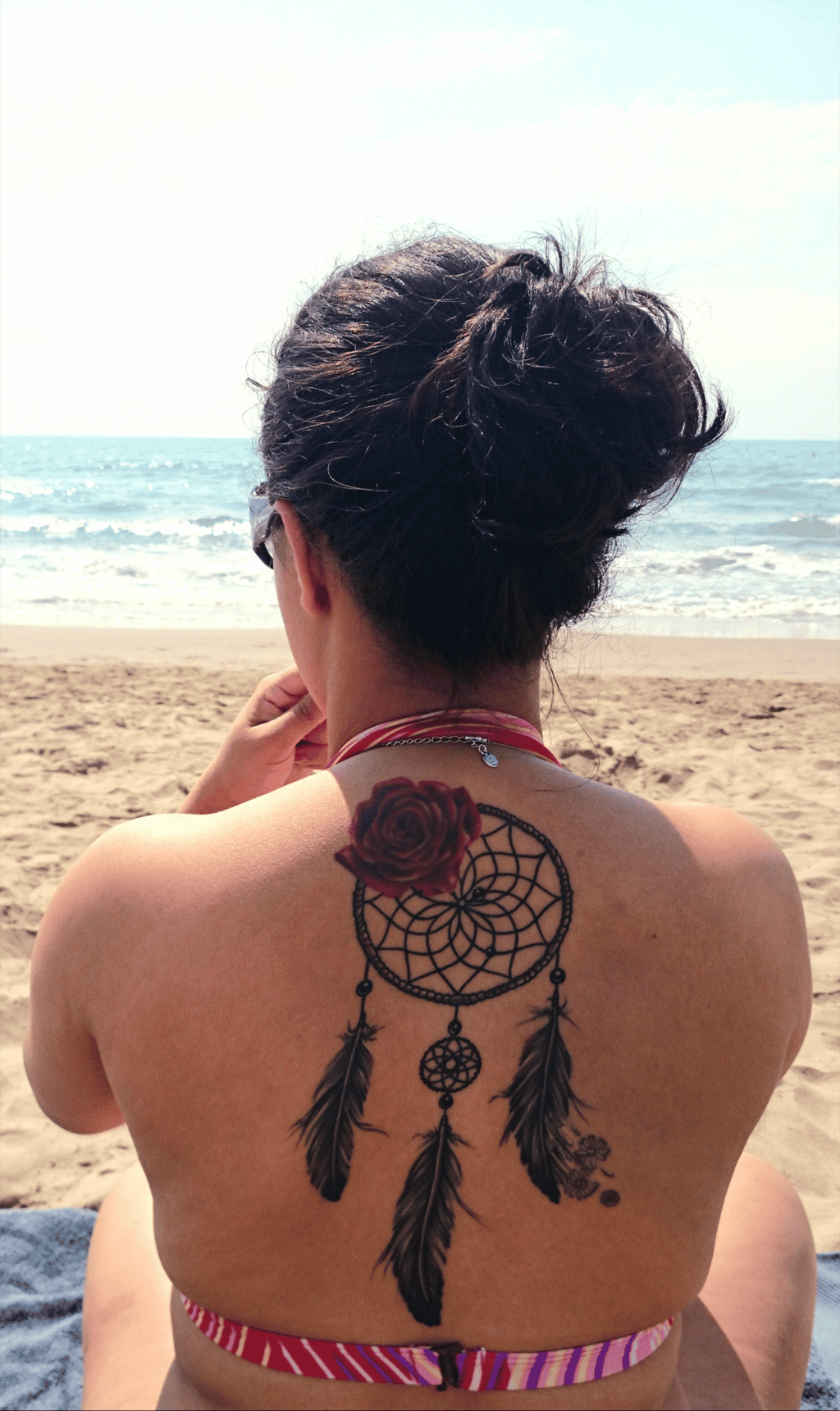 Femme de dos sur la plage, tatouage de rose et capteur de rêves, symbole de mémoire et lignée spirit
