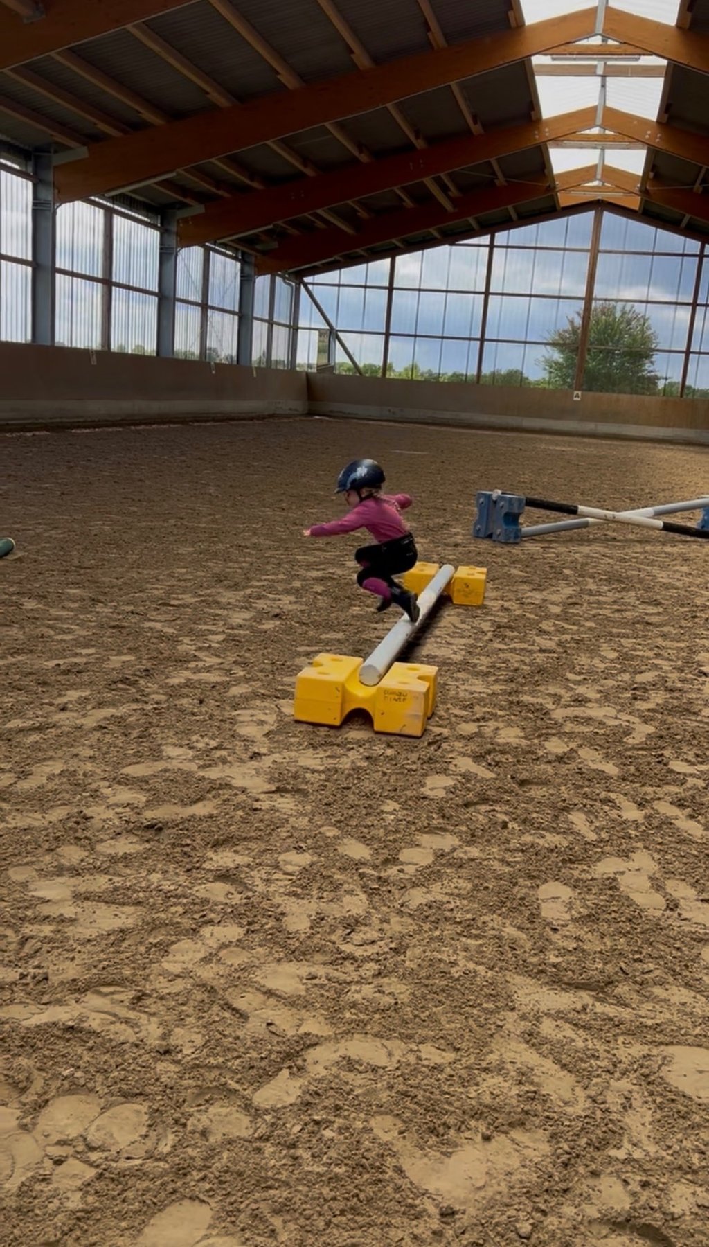 Young child in a riding helmet jumping over a hurdle in an indoor horse riding arena. Ponytante