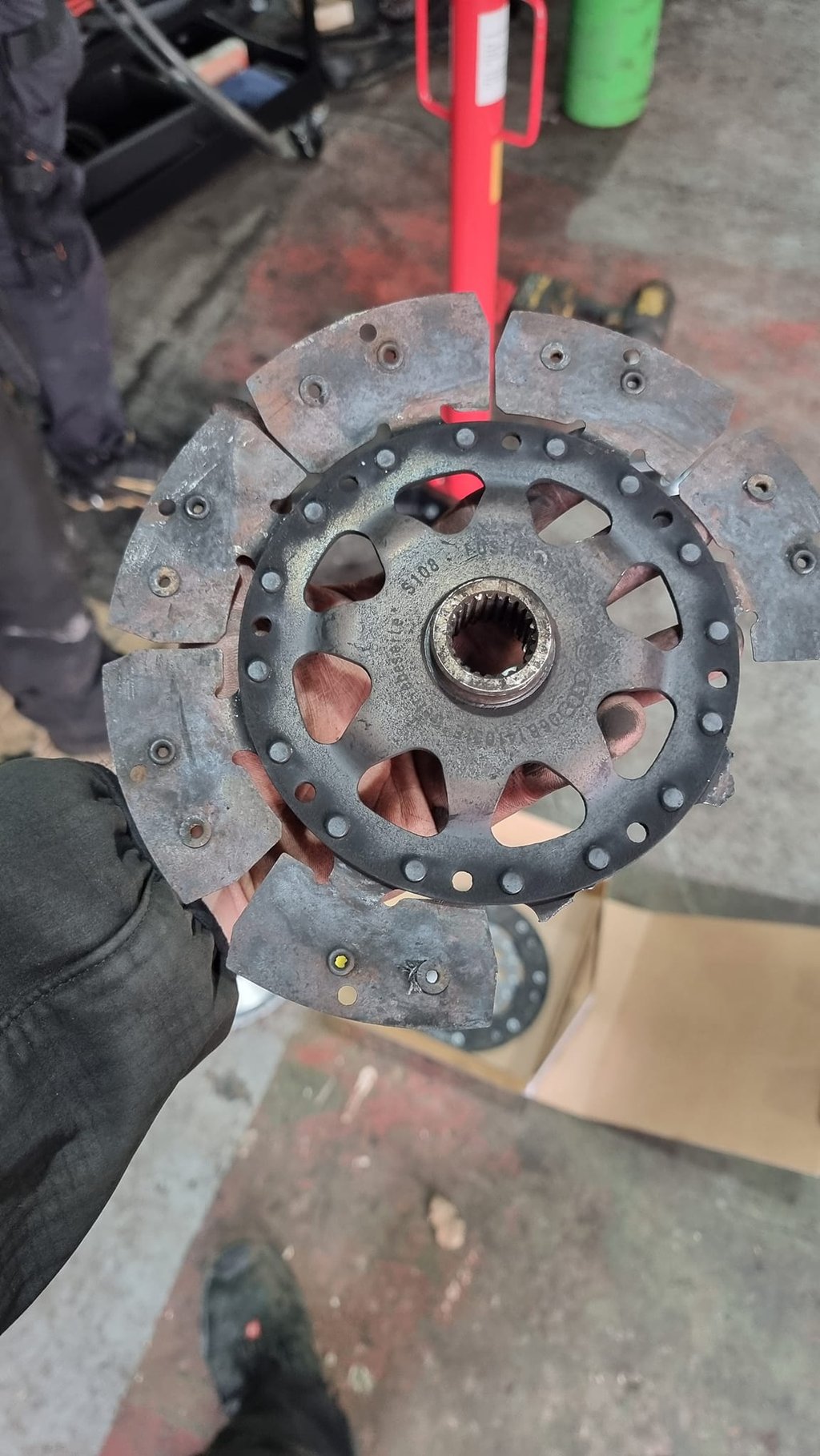A mechanic holding a worn and damaged automotive clutch friction disc in a repair shop.
