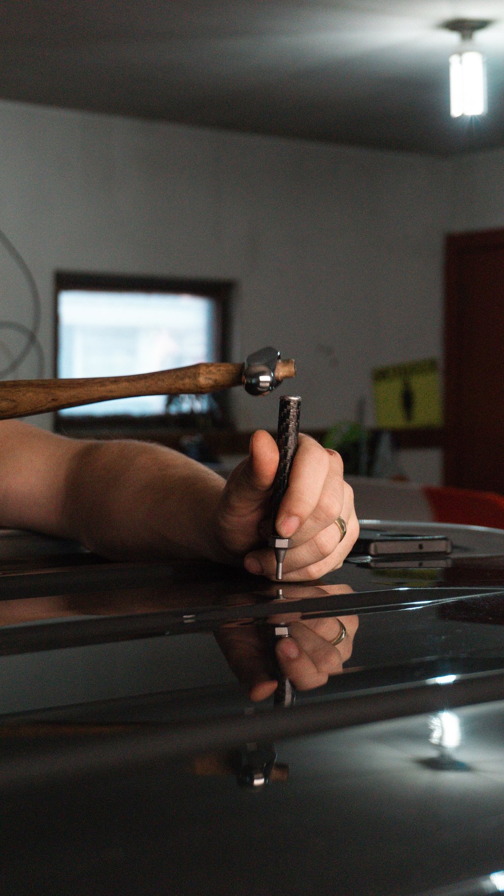 Professional technician using a hammer and punch tool for paintless dent repair on a black car.