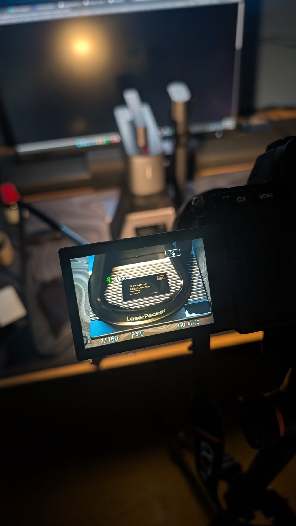 Camera screen previewing a LaserPecker engraving machine setup in a dark home office studio.