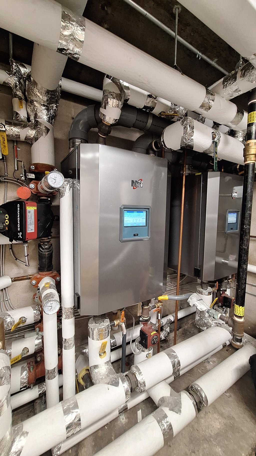 Commercial high-efficiency NTI gas boilers with insulated pipes and digital controls in a utility room.