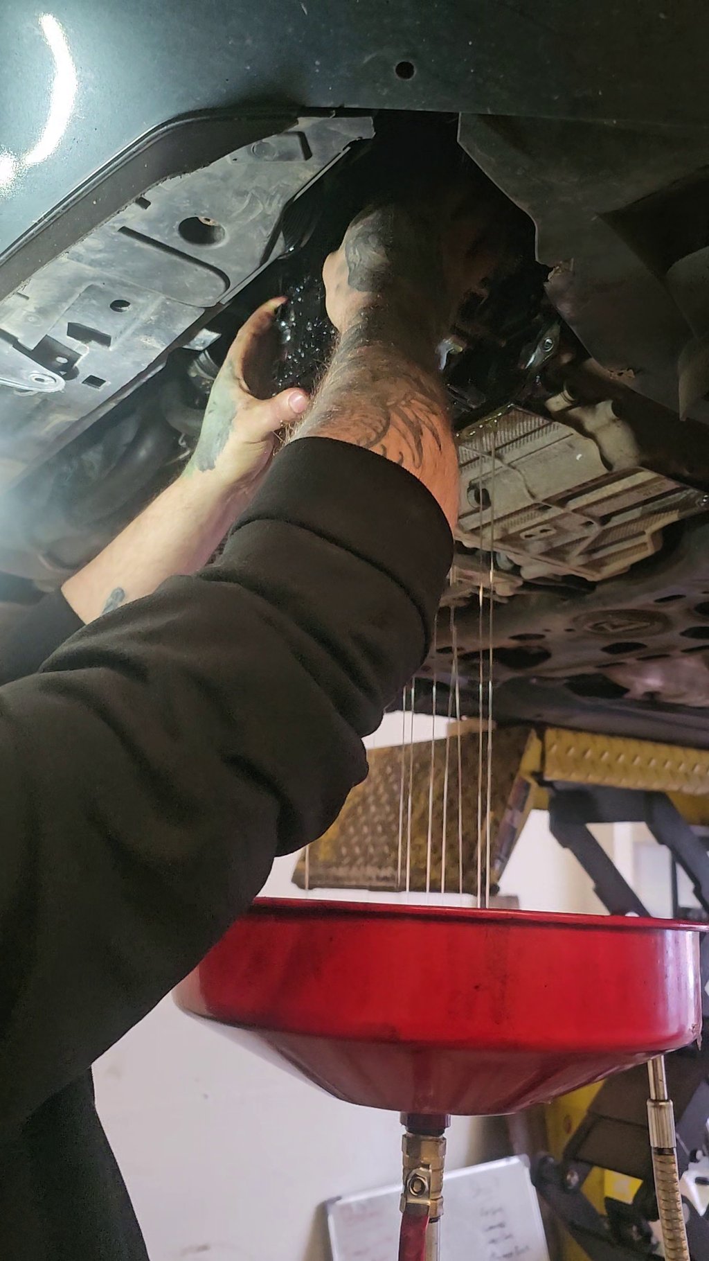 A mechanic draining old oil into a red collection pan during a mechatronic repair