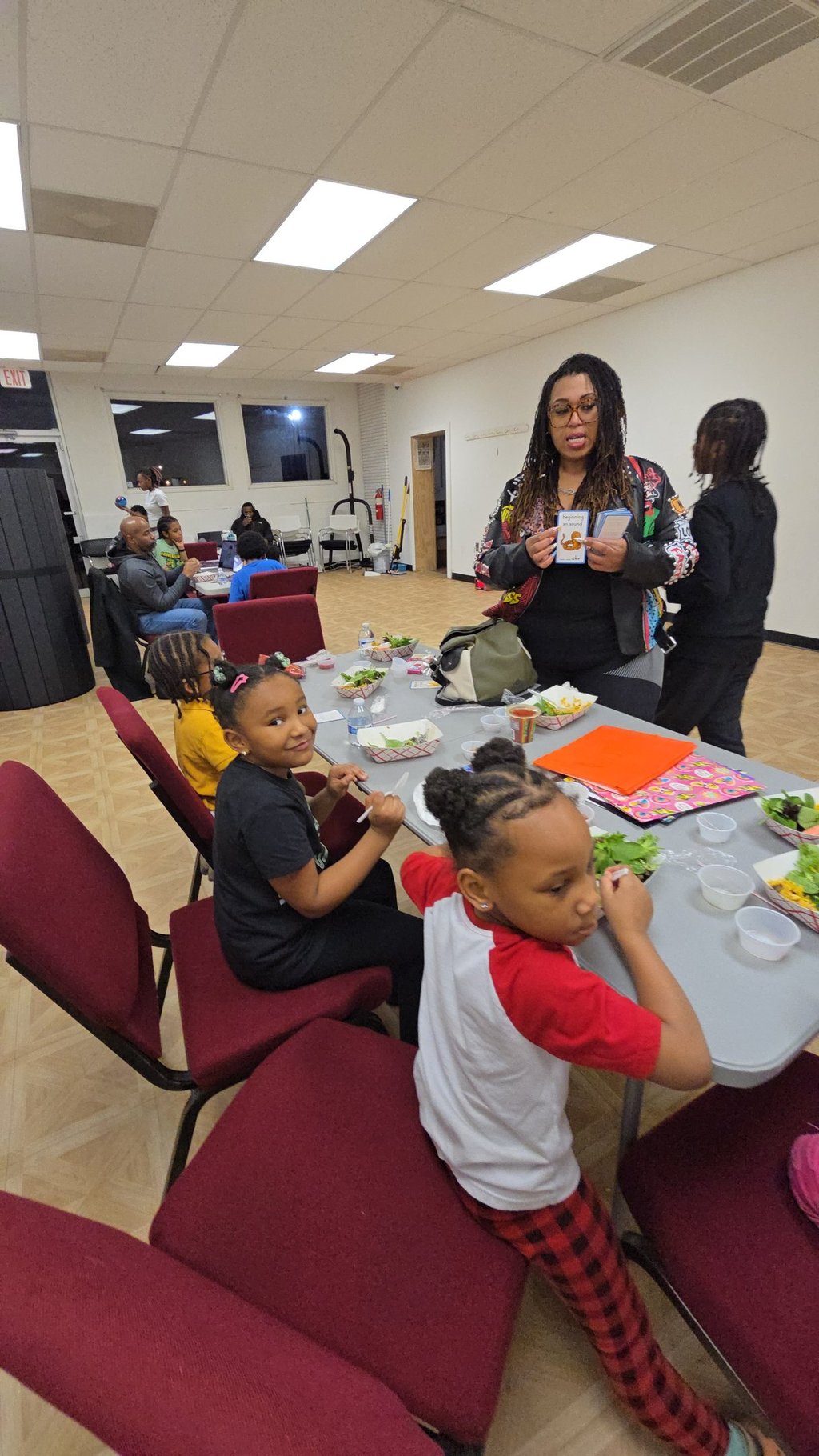 A group of children and adults participating in a community workshop with healthy meals and educational cards.